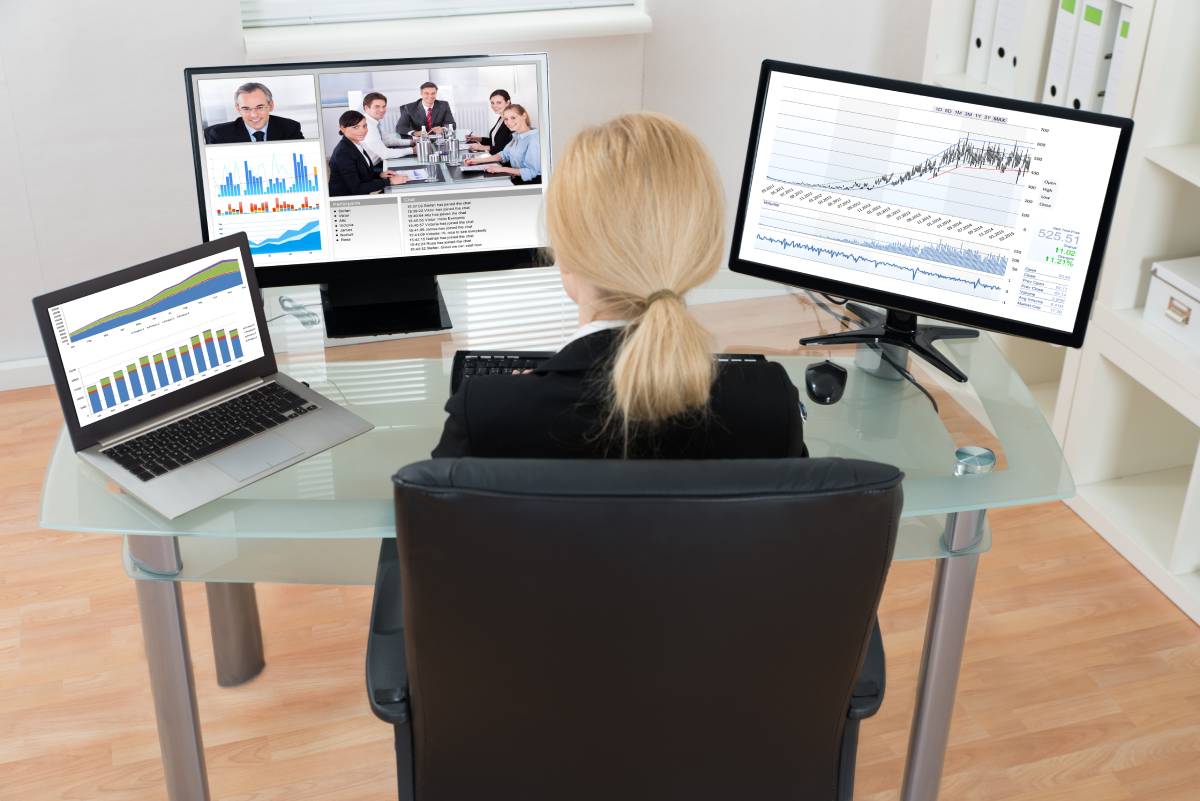 Woman sitting at a desk with three monitors, collaborating with coworkers via video conference