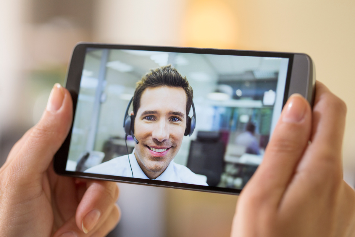 Woman's Hands Holding Cell Phone on Video Call with Smiling Male Customer Service Representative Wearing Headset