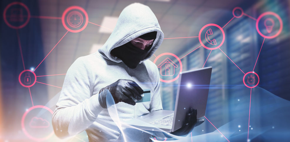 Masked and hooded man holding credit card and a laptop