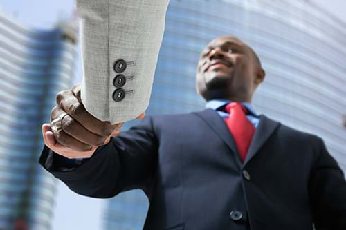 Man in Dark Suit Shaking Hands with Another Man Off Camera in Front of Highrise Building, Business Partnership Concept