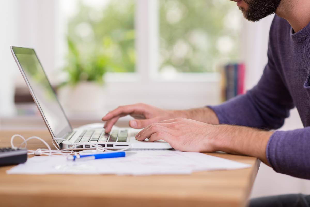 A man working remotely at his desk and using a laptop