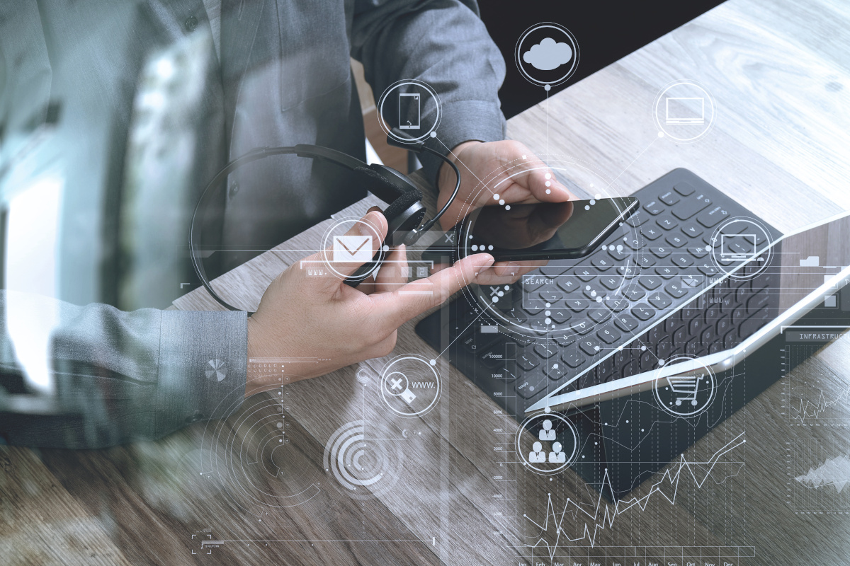 Close up of someone holding a phone in one hand and a headset casually in the other in front of their tablet.