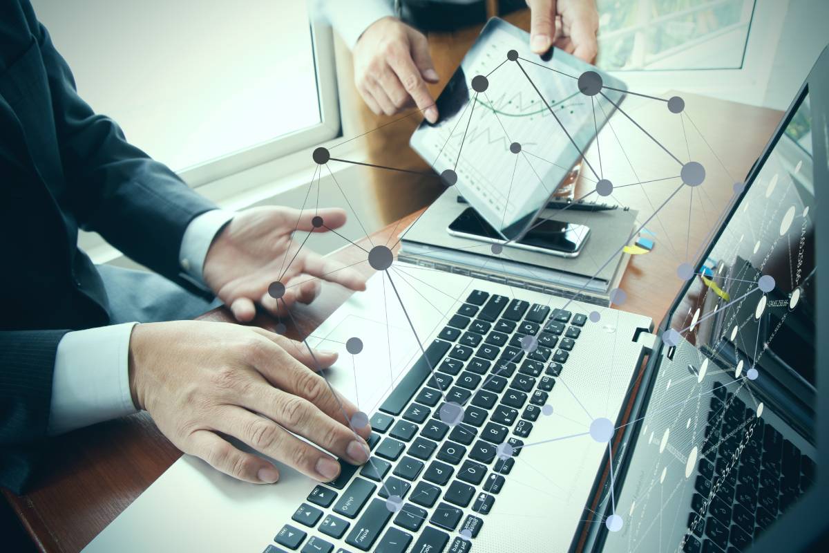 A businessman working at his computer with another businessman showing him a graph on a tablet