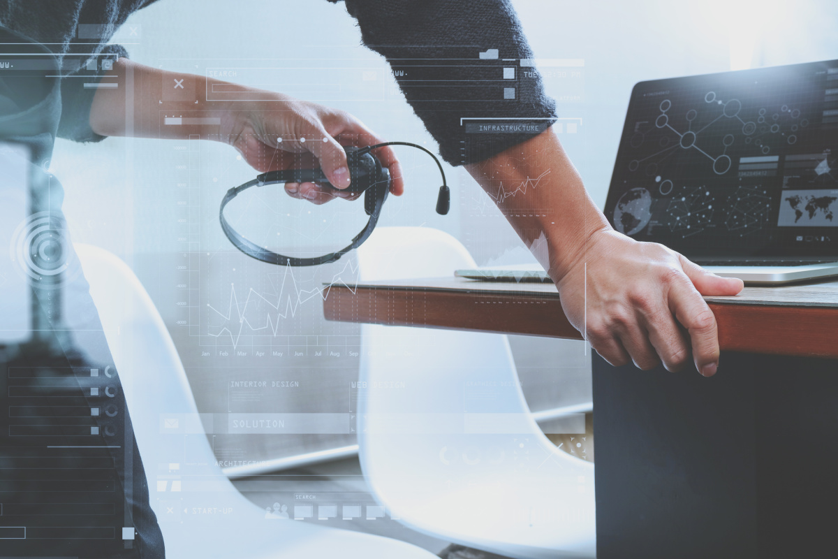 Close up of businessman holding headset with microphone while using laptop computer. Cloud voice concept.