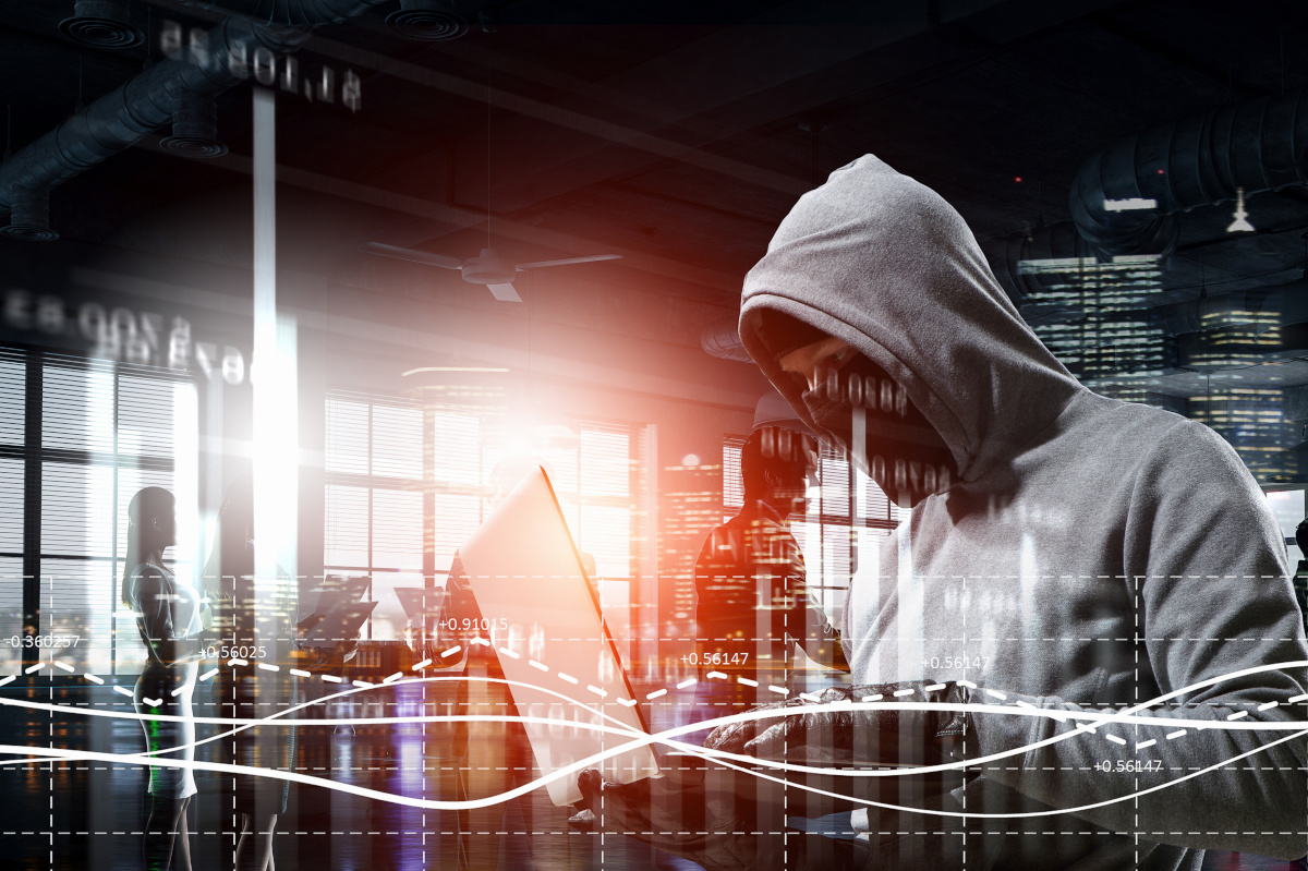 A hacker wearing a white hooded sweatshirt stealing information from a laptop