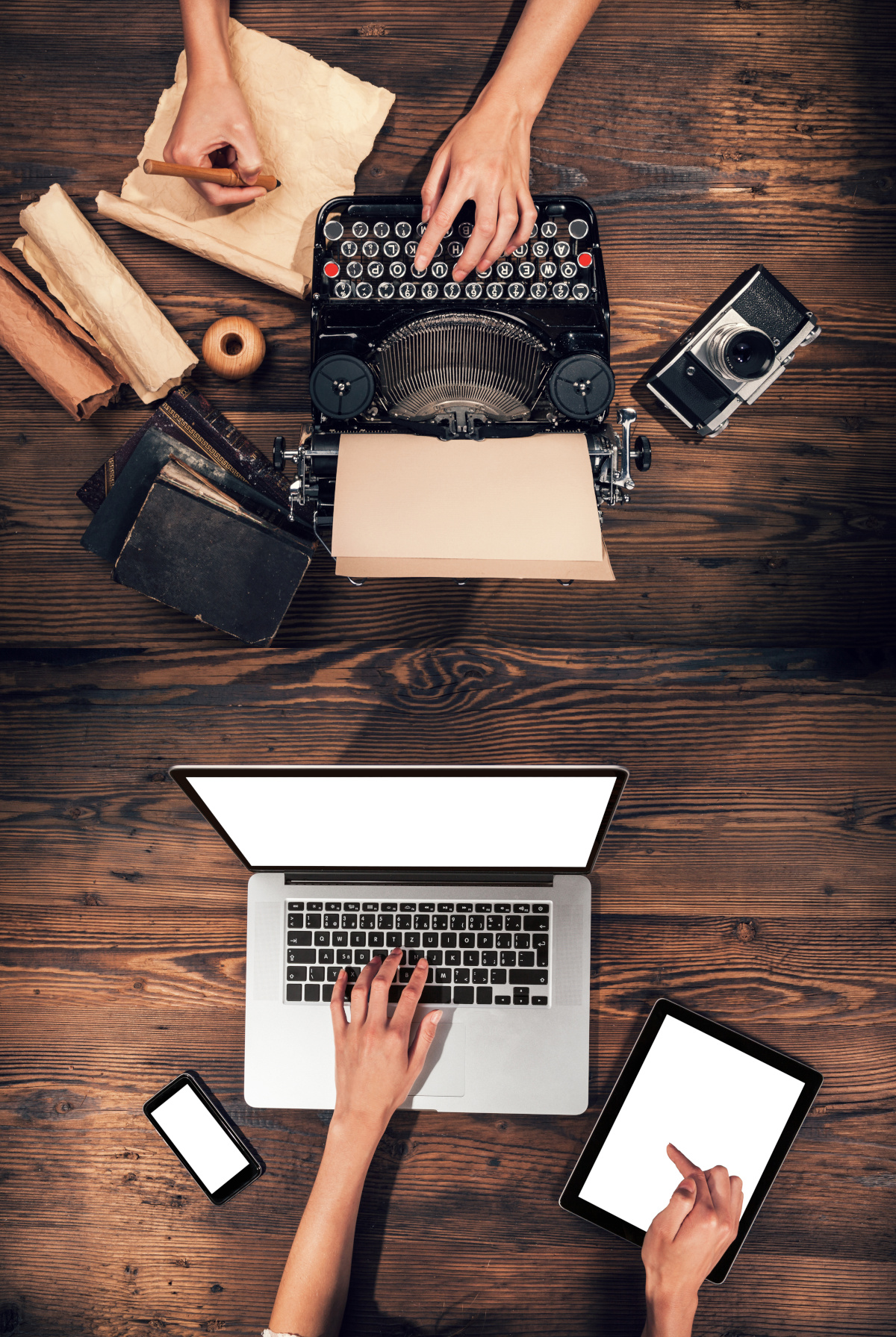 Two people sitting across from one another, one using an old typewriter and the other using a modern laptop.