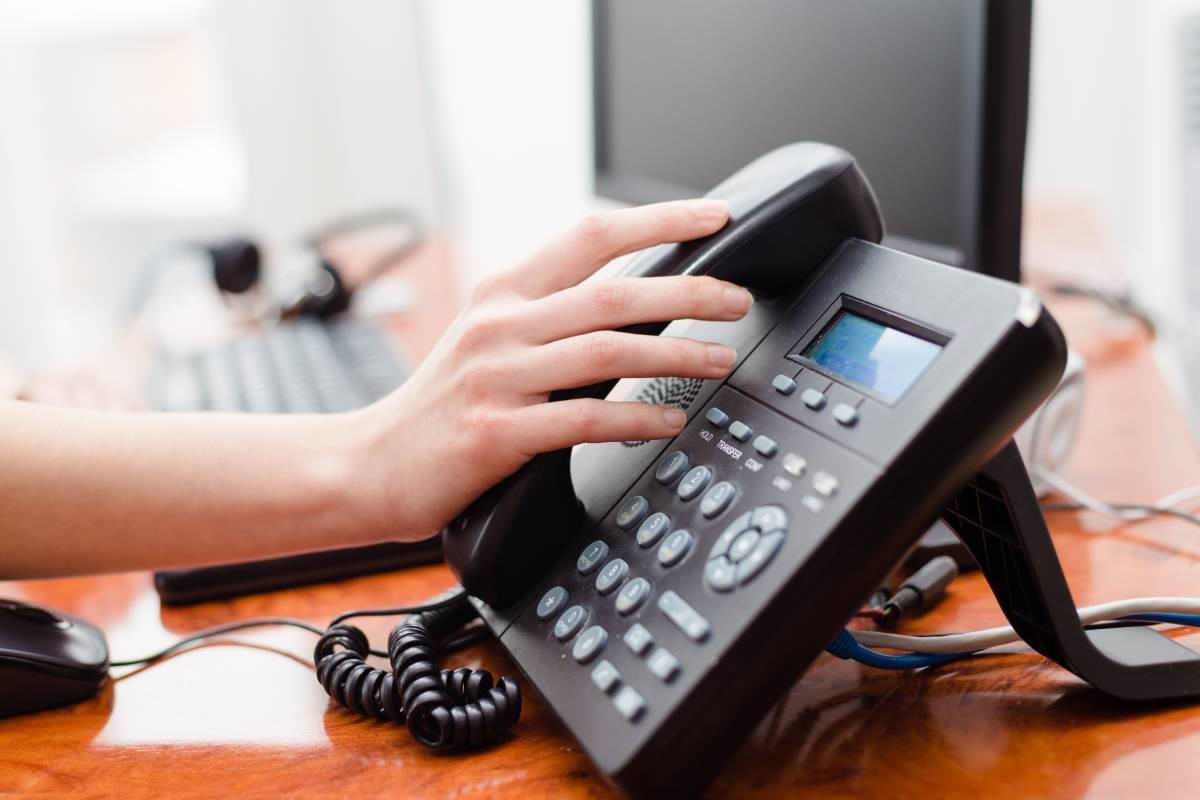 A hand grabbing an office desk phone