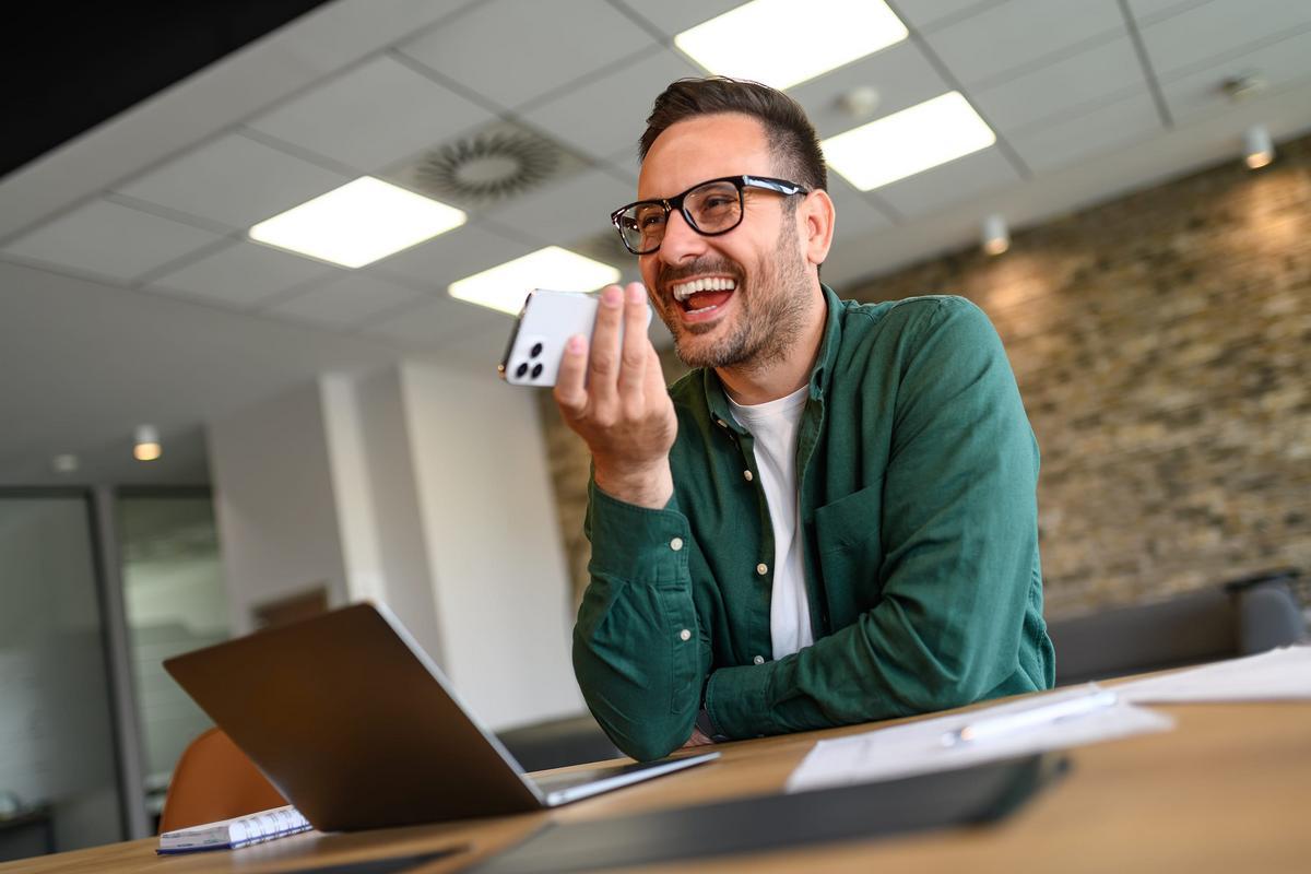 Business professional smiling while speaking on a phone at his desk.